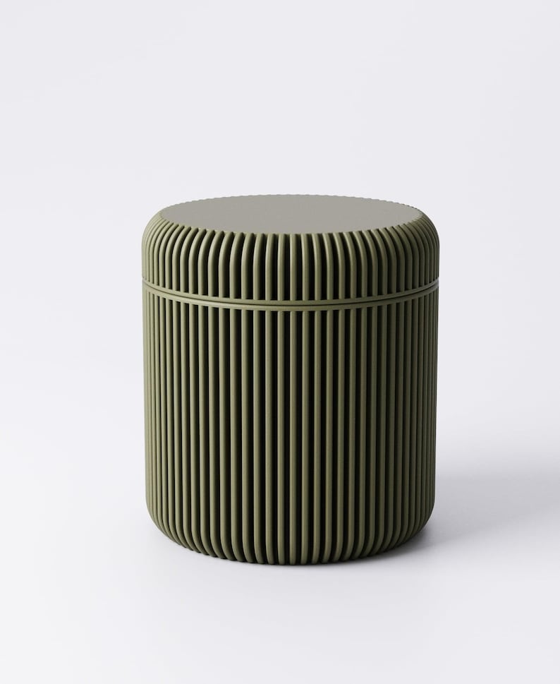 May include: A cylindrical container in a muted olive green hue. The container features a ridged, vertical design on its exterior, with a matching lid. The overall shape is rounded, and the design is minimalist and modern.