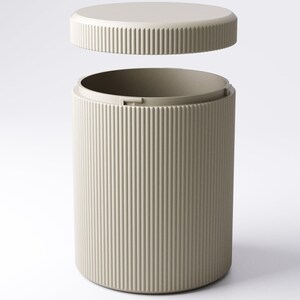 May include: A beige cylindrical container with a matching lid. The container and lid have vertical ribbed detailing. The lid is slightly elevated above the container, suggesting it is removable. The design is minimalist and modern.