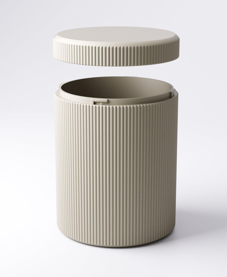 May include: A beige cylindrical container with a matching lid. The container and lid have vertical ribbed detailing. The lid is slightly elevated above the container, suggesting it is removable. The design is minimalist and modern.