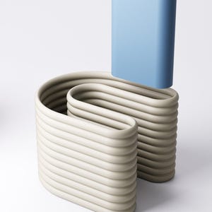May include: An abstract sculpture comprising two beige, wave-like forms and a light blue, rectangular vase. The beige forms have a ribbed texture, while the blue vase is smooth. The artwork is set against a white backdrop.