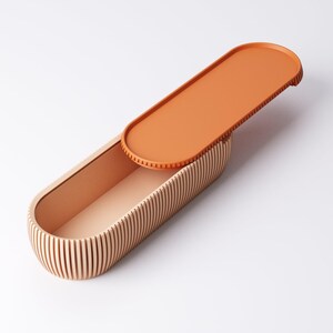 May include: An open, oval-shaped wooden box with a lid. The box is made of light-colored wood with vertical grooves on the sides. The lid is a solid orange color and is partially open, revealing the interior of the box. The interior is a light peach color.