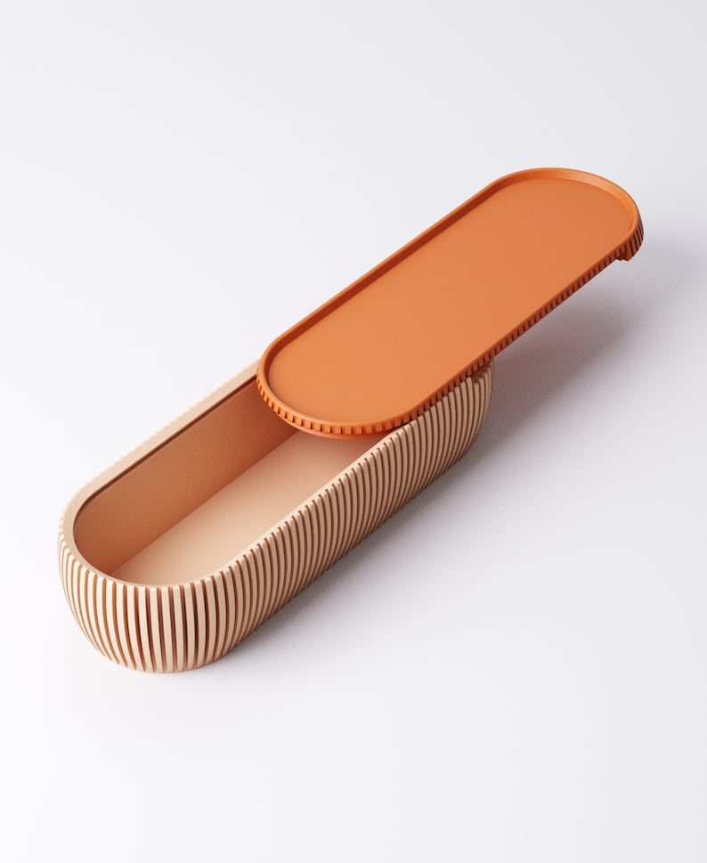 May include: An open, oval-shaped wooden box with a lid. The box is made of light-colored wood with vertical grooves on the sides. The lid is a solid orange color and is partially open, revealing the interior of the box. The interior is a light peach color.