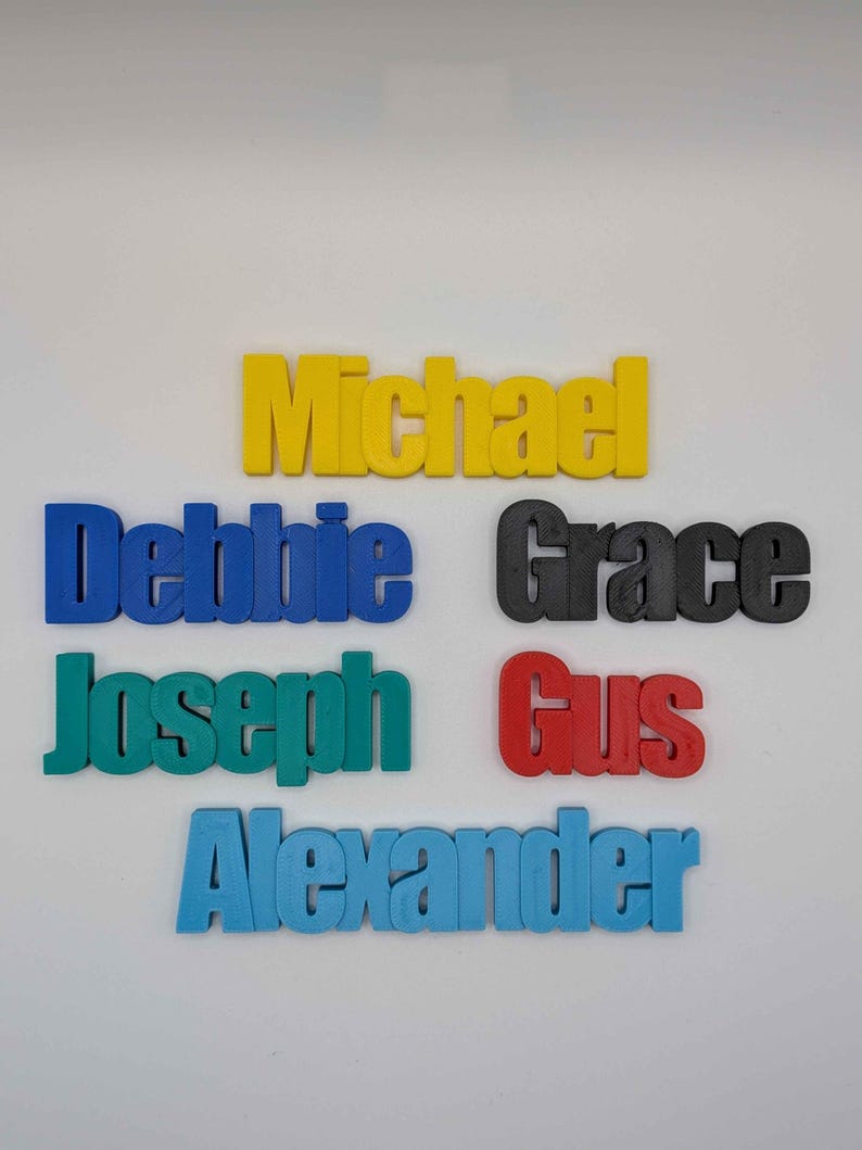 May include: A collection of colorful 3D-printed names: Michael in yellow, Debbie in blue, Grace in black, Joseph in teal, Gus in red, and Alexander in light blue. The names are displayed on a white background.