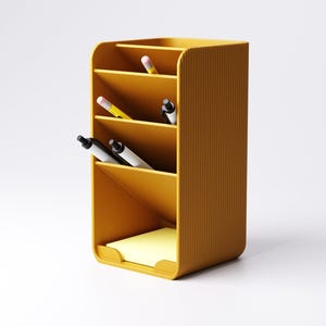 May include: Mustard yellow desk organizer with multiple compartments. The organizer holds pens, pencils, and a pad of yellow sticky notes. The exterior has a ribbed texture. The design is modern and minimalist, suitable for office or home use.