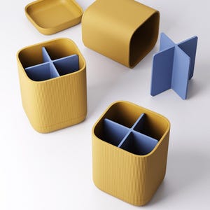 May include: A set of mustard yellow desk organizers with a ribbed texture. The set includes two square containers with blue dividers, a square lid, and a separate blue cross-shaped divider. The organizers are designed for office or home use.