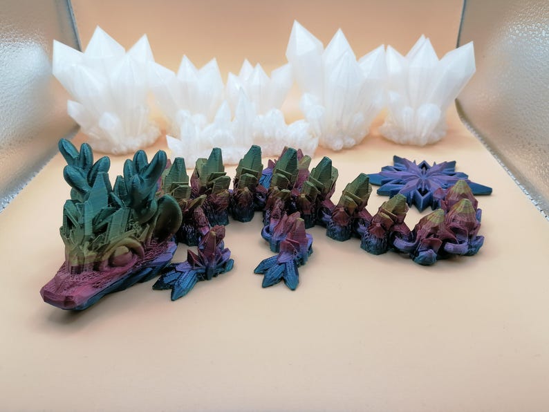 May include: A collection of 3D-printed crystal formations in various sizes and colors. The foreground features a multi-colored, segmented crystal structure with blue, purple, and green hues. Several white crystal clusters are in the background.
