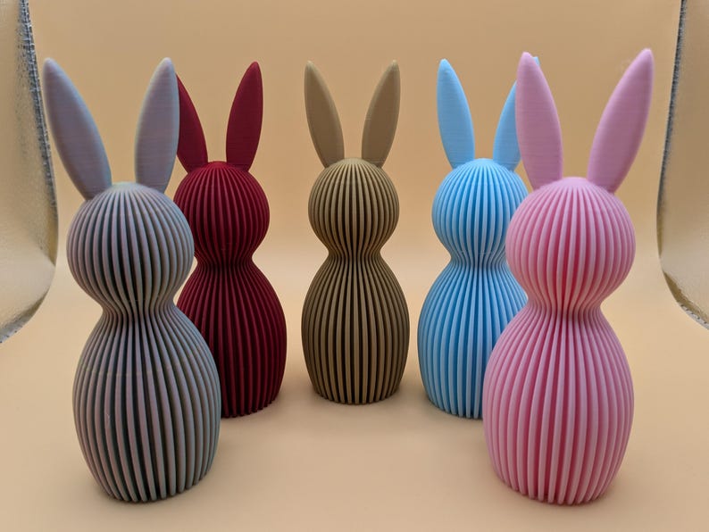 K&ouml;nnte beinhalten: Eine Sammlung von sechs dekorativen Hasenfiguren in verschiedenen Farben. Die Hasen sind vertikal gestreift und haben lange Ohren. Zu den Farben geh&ouml;ren Grau, Burgunderrot, Beige, Blau und Rosa. Die Figuren sind etwa 15 cm hoch.