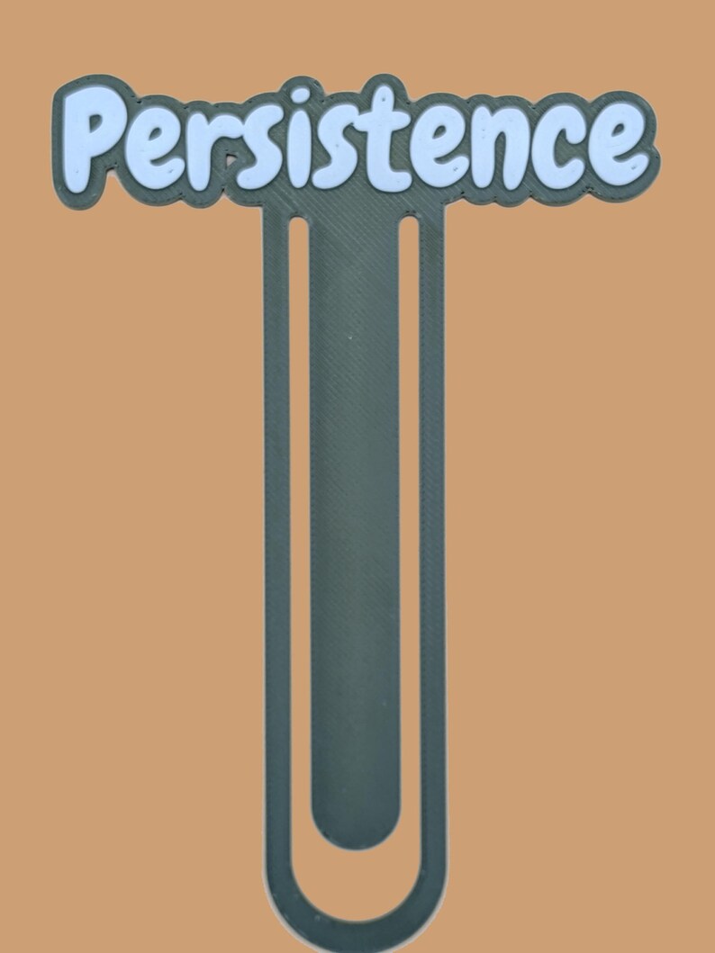 May include: A dark grey bookmark shaped like a large paperclip with the word Persistence written in light blue, rounded, bubble-style letters across the top horizontal bar. The design features a clean, matte finish and a simple, functional structure.