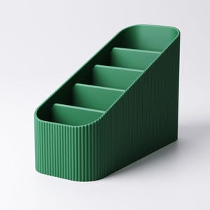 May include: A green desk organizer with a ribbed exterior and four interior compartments. The organizer has a slanted design, with the compartments increasing in height. The color is a deep, saturated green.