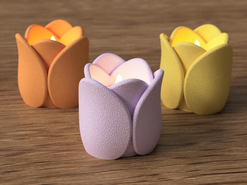 May include: Three tulip-shaped candle holders in orange, lavender, and yellow. Each holder has a lit candle inside, casting a warm glow. The holders are made of a textured material and sit on a wooden surface.