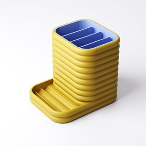 May include: A yellow and blue desk organizer with a unique, ribbed design. The organizer has a rectangular shape with a tray on the side. The interior is divided into four sections, and the tray has a ribbed surface.