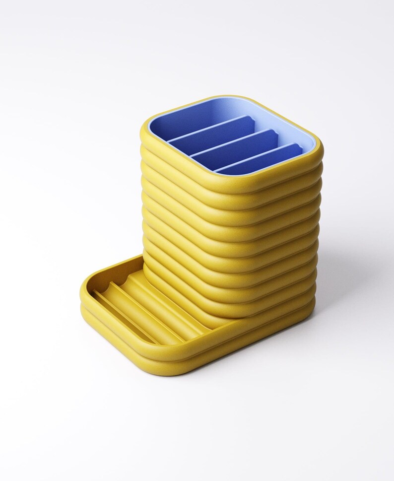 May include: A yellow and blue desk organizer with a unique, ribbed design. The organizer has a rectangular shape with a tray on the side. The interior is divided into four sections, and the tray has a ribbed surface.