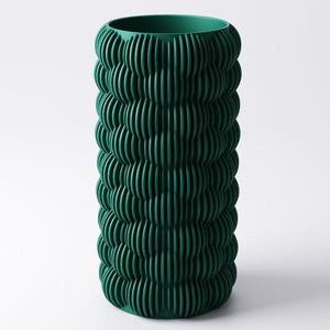 May include: A tall, cylindrical vase in a deep forest green hue. The vase features a textured, ribbed design that wraps around the entire body. The vertical ridges create a pattern of light and shadow, adding visual interest to the decorative piece.