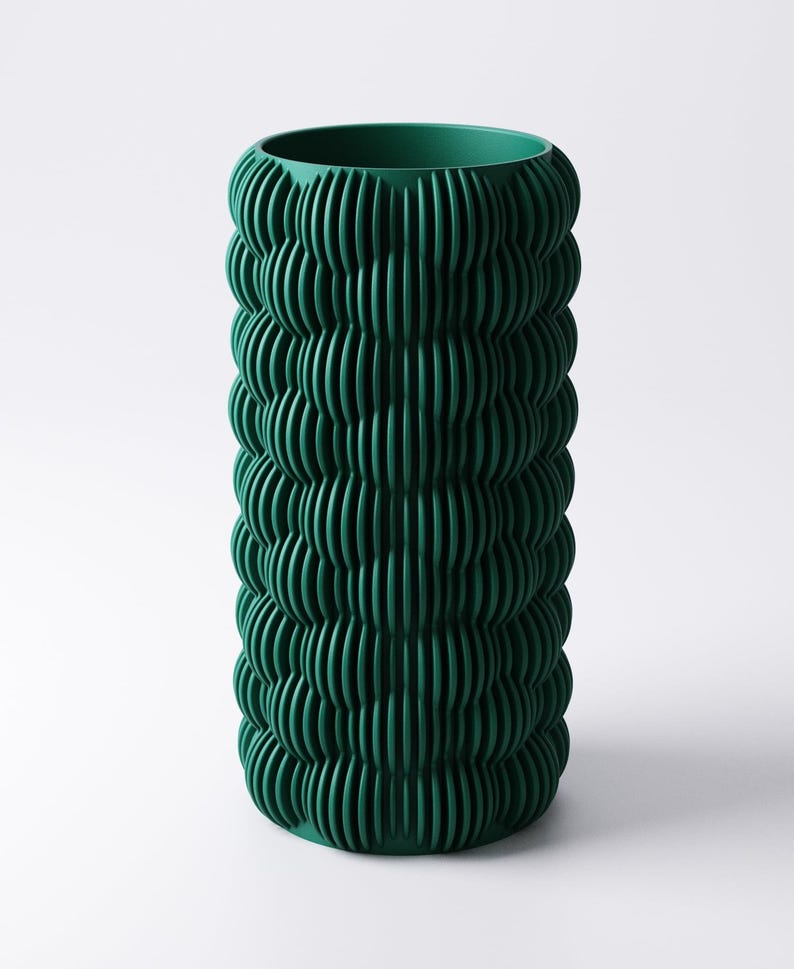 May include: A tall, cylindrical vase in a deep forest green hue. The vase features a textured, ribbed design that wraps around the entire body. The vertical ridges create a pattern of light and shadow, adding visual interest to the decorative piece.