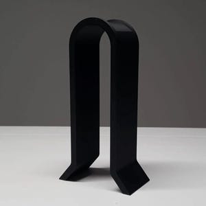 K&ouml;nnte beinhalten: Ein schwarzer Buchst&uuml;tze im modernen Stil mit gew&ouml;lbter Oberseite und zwei vertikalen St&uuml;tzen. Die Buchst&uuml;tze besteht aus einem soliden, matten Material und hat ein minimalistisches Design. Die Basis der Buchst&uuml;tze hat eine geometrische Form.