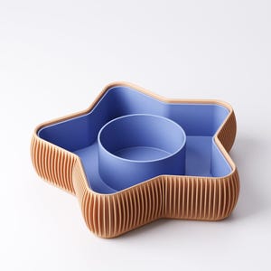 May include: A star-shaped serving dish with a blue interior and a light brown, ribbed exterior. The dish has a central, circular compartment and is designed for serving snacks or appetizers.
