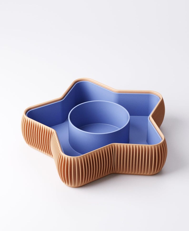 May include: A star-shaped serving dish with a blue interior and a light brown, ribbed exterior. The dish has a central, circular compartment and is designed for serving snacks or appetizers.