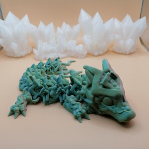 May include: A 3D-printed sculpture of a stylized wolf in shades of green and blue, with a textured, organic appearance. Above, several white, crystalline formations resemble clusters of quartz. The objects are displayed on a neutral background.