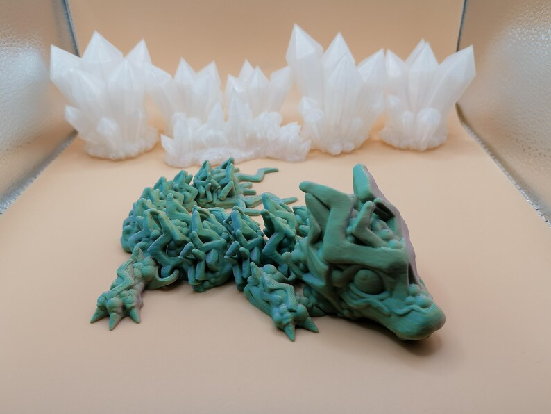 May include: A 3D-printed sculpture of a stylized wolf in shades of green and blue, with a textured, organic appearance. Above, several white, crystalline formations resemble clusters of quartz. The objects are displayed on a neutral background.