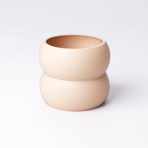 May include: A peach-colored ceramic vase with a unique, rounded shape. The vase is composed of two stacked, spherical sections, creating a bulbous form. The smooth, matte finish and neutral color make it a versatile decorative item.