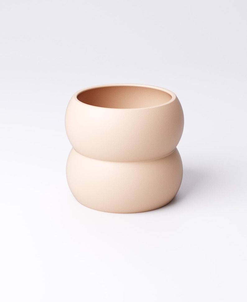 May include: A peach-colored ceramic vase with a unique, rounded shape. The vase is composed of two stacked, spherical sections, creating a bulbous form. The smooth, matte finish and neutral color make it a versatile decorative item.