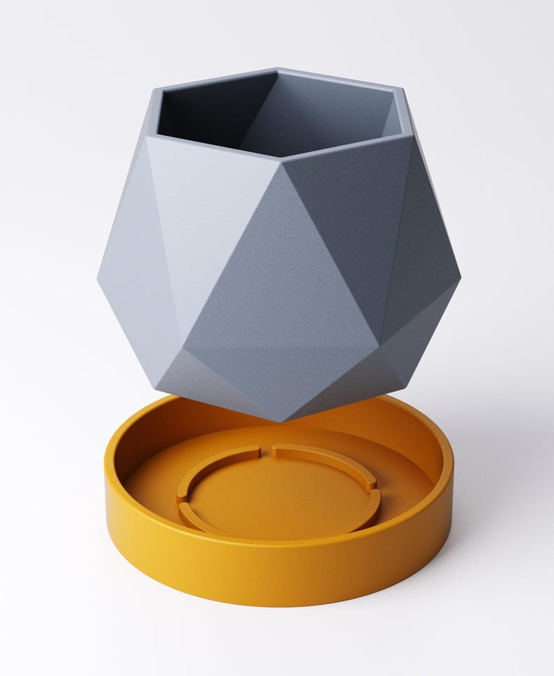 May include: A geometric, gray planter with a faceted design, hovering above a round, mustard-yellow saucer. The planter has a hexagonal opening and is made of a matte material. The saucer has a circular indentation.