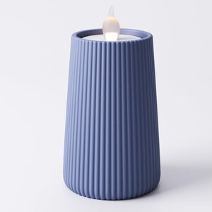 May include: A blue candle holder with vertical ribbed detailing. The candle holder has a tapered shape and a small, flickering LED light at the top, resembling a flame. The candle holder is a solid blue color.