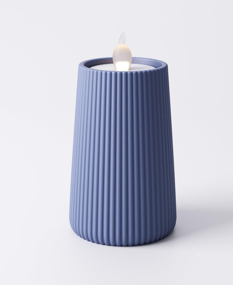 May include: A blue candle holder with vertical ribbed detailing. The candle holder has a tapered shape and a small, flickering LED light at the top, resembling a flame. The candle holder is a solid blue color.