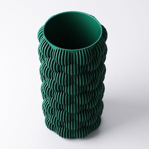 May include: A tall, cylindrical vase in a deep forest green hue. The vase features a textured, ridged design that wraps around the entire body. The opening at the top is circular, and the vase stands on a white background.