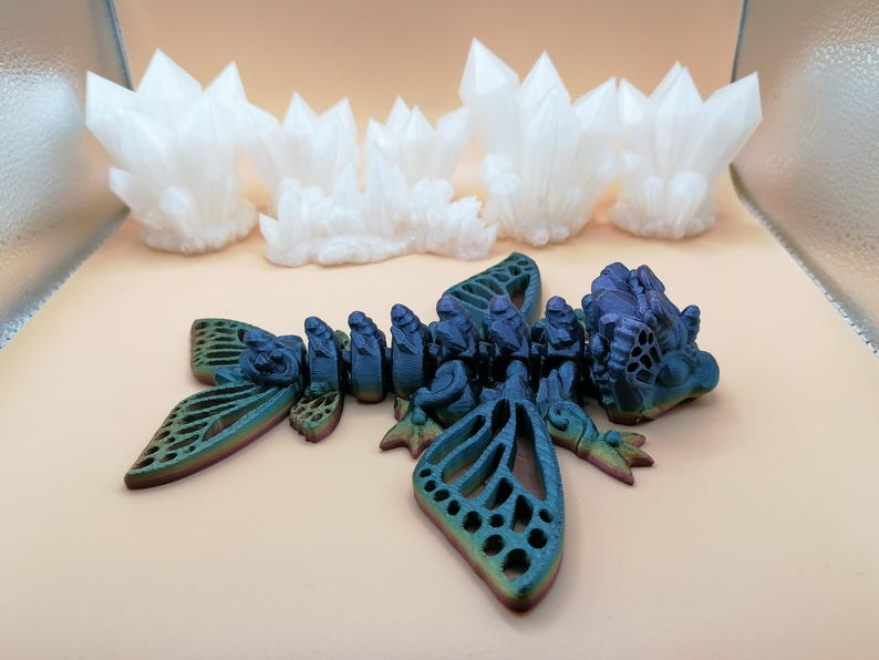 May include: A multi-colored, articulated dragon figurine with intricate details, including openwork wings and a segmented body. The dragon is in shades of blue, green, and purple. In the background are several white crystal formations.