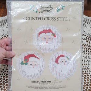 May include: A sealed plastic package containing a counted cross stitch kit. The kit features three Santa Claus ornaments with red hats and white beards. The text "Something Special" and "COUNTED CROSS STITCH" are visible.