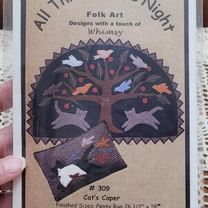 May include: A craft pattern packet titled All Through the Night featuring a tree with birds and two cats, plus a plaid pillow design. Text includes # 309 Cat's Caper, Finished Sizes: Penny Rug 26 1/2" x 18", Pillow: 17" x 11", and ©2003.