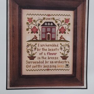 May include: Cross-stitch pattern for a small house with a red door and windows, surrounded by flowers and bees. The text reads "I am humbled by the beauty of a flower in the breeze surrounded by an orchestra of softly buzzing bees". The pattern is titled "Little House Chart No. Thirty-Seven".