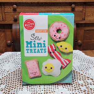 May include: A box of "Best of Sew Mini Treats" by Klutz. The box features a green plate with a pink donut, a lemon, bacon, a fried egg, and a pink frosted toast. The box is 100% Klutz certified.