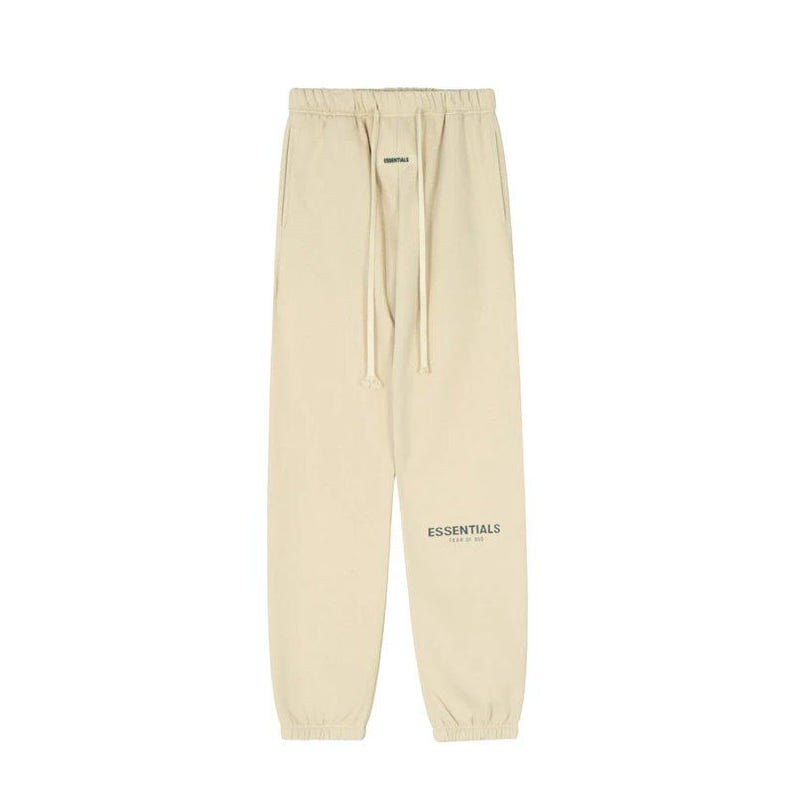 May include: Tan sweatpants with a drawstring waist and the word "ESSENTIALS" printed on the left leg. The pants are made of a soft material and have a relaxed fit. The pants are a neutral color.
