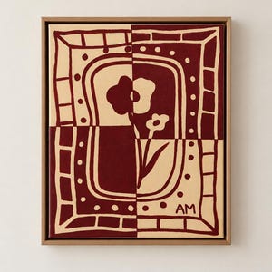 Puede incluir: Un cuadro rectangular sobre lienzo en un marco de madera clara con un dise&ntilde;o bicolor en rojo oscuro y crema. La obra muestra una flor estilizada centrada dentro de un borde decorativo de cuadrados y puntos, con las letras AM en la esquina.