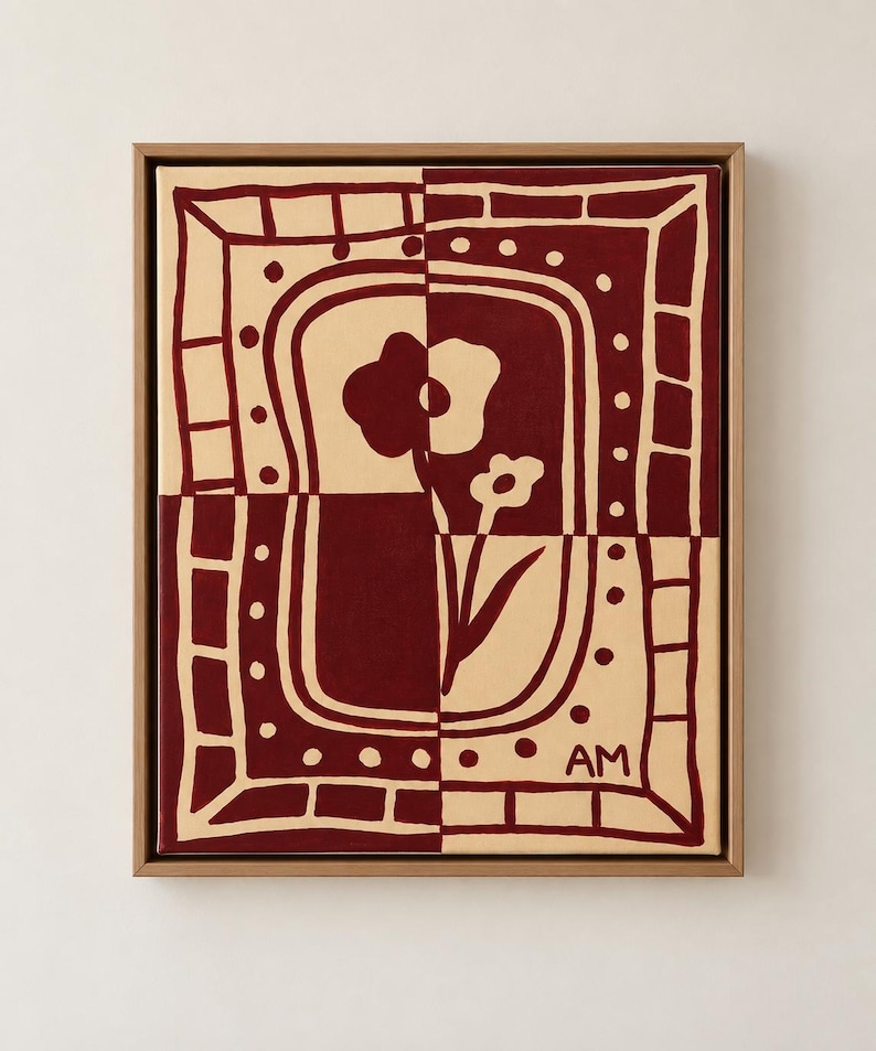 Puede incluir: Un cuadro rectangular sobre lienzo en un marco de madera clara con un dise&ntilde;o bicolor en rojo oscuro y crema. La obra muestra una flor estilizada centrada dentro de un borde decorativo de cuadrados y puntos, con las letras AM en la esquina.