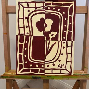 Puede incluir: Un cuadro rectangular sobre lienzo con un dise&ntilde;o bicolor en granate oscuro y crema. La obra muestra un motivo floral estilizado dentro de un borde decorativo de rect&aacute;ngulos y puntos. Las letras AM est&aacute;n pintadas en la esquina inferior derecha.