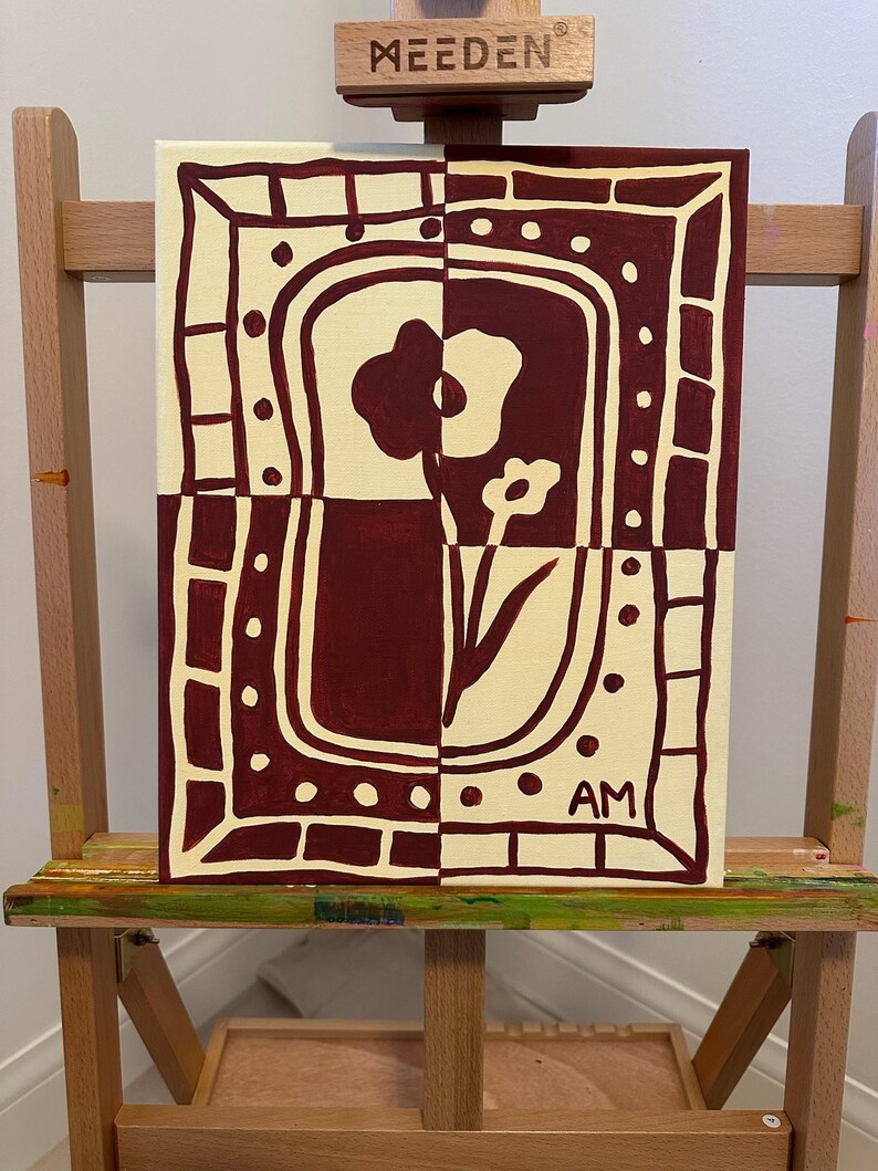 Puede incluir: Un cuadro rectangular sobre lienzo con un dise&ntilde;o bicolor en granate oscuro y crema. La obra muestra un motivo floral estilizado dentro de un borde decorativo de rect&aacute;ngulos y puntos. Las letras AM est&aacute;n pintadas en la esquina inferior derecha.