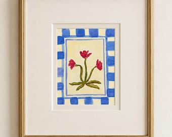 Puede incluir: Una pintura en acuarela enmarcada que muestra tres flores rojas con tallos verdes sobre un fondo amarillo pálido, rodeada por un borde a cuadros azules y blancos, dentro de un marco dorado con un paspartú blanco.