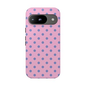 May include: A pink phone case with a pattern of blue polka dots. The case has a camera cutout and side buttons. The phone case is designed to fit a specific phone model.