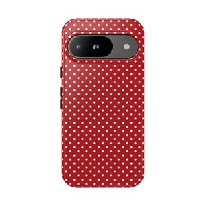 May include: Red phone case with a white polka dot pattern. The case has a camera cutout and side buttons. The phone case is designed to fit a smartphone.