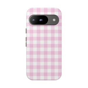 May include: A phone case with a pink and white gingham pattern. The case has a camera and flash cutout at the top and black buttons on the side. The case is designed to fit a smartphone.