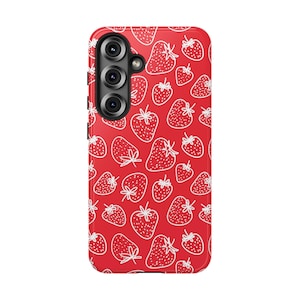 May include: A red phone case featuring a repeating pattern of white outlined strawberries. The case has a camera module with three lenses on the upper left. Strawberries of various sizes are scattered across the surface.