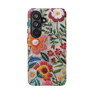 May include: A phone case with a floral embroidery design. The case features a variety of colorful flowers in shades of red, orange, pink, and yellow, with green leaves and stems. The background is a light beige color.