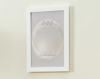 May include: A white framed print with a gray background featuring a large circle with the text "000" and the words "limitless divinity" written below the circle.