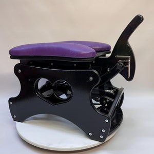 May include: A black wooden chair with a purple padded seat and a heart-shaped cutout in the back. The chair is on a white rotating base.