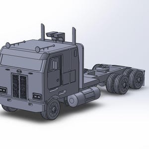 May include: A grey 3D model of a semi-truck cab featuring a flat front design, a prominent vertical grille, dual exhaust stacks, and a tandem rear axle configuration. The vehicle includes side fuel tanks and a hitch assembly on the chassis frame.