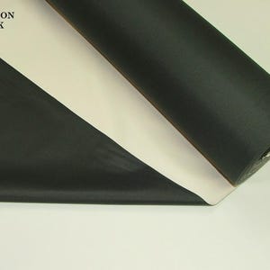 May include: A roll of black fabric with a white backing. The fabric is unrolled to reveal a portion of the black material. The words "FASHION TRACK" are visible in the upper left corner.