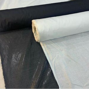 Könnte beinhalten: Bild von Stoffrollen in Schwarz und Weiß. Der schwarze Stoff ist strukturiert und glänzend, während der weiße Stoff glatt ist. Die Rollen liegen auf einem weißen Tuch.